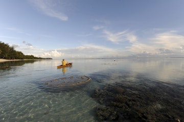 Man paddling canoe on Raratonga coast.