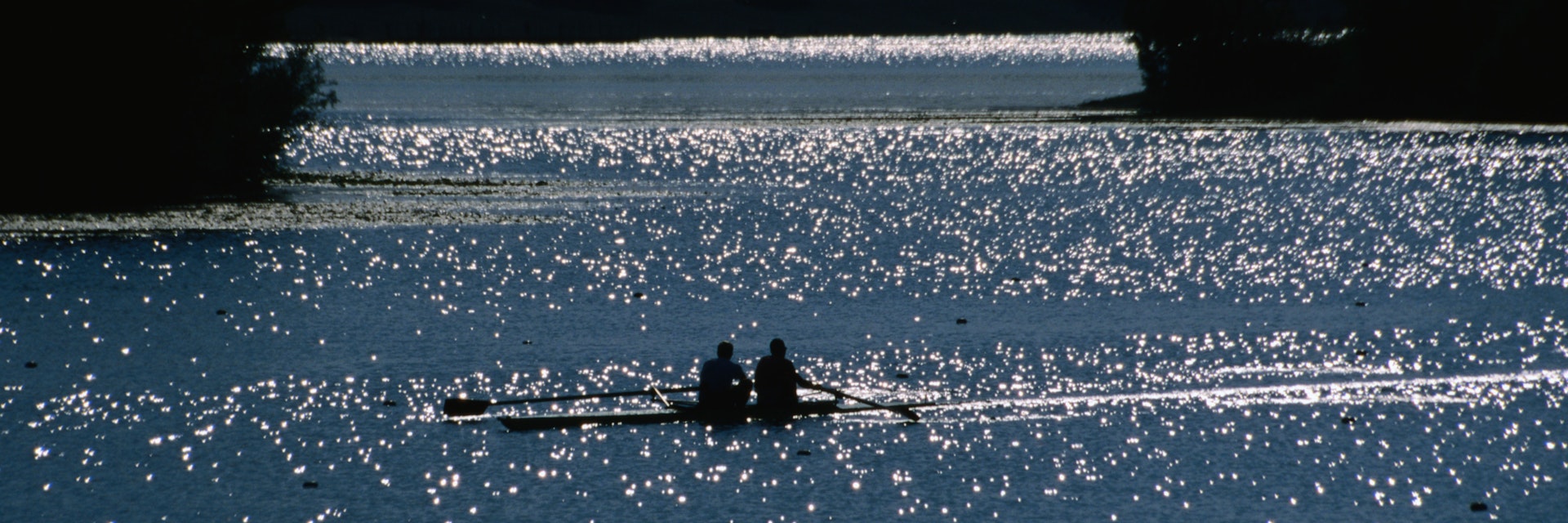 Two rowers propelling their craft through the sun-dappled waters of Jarun Lake.