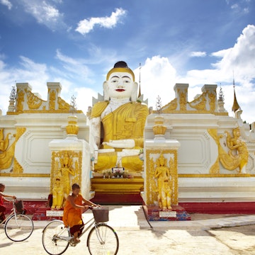 Novice monks cycling past 26-foot high sitting Buddha at Yan Aung Nan Aung Hsu Taung Pyi Pagoda near Inle Lake.