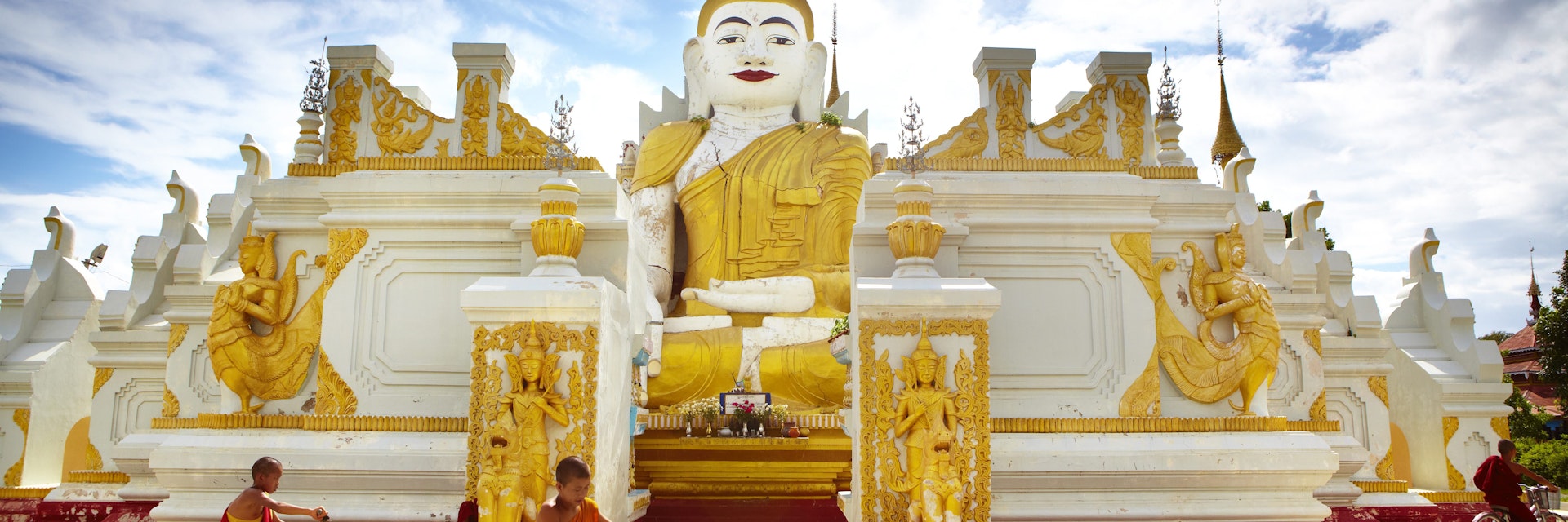Novice monks cycling past 26-foot high sitting Buddha at Yan Aung Nan Aung Hsu Taung Pyi Pagoda near Inle Lake.