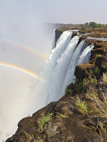 Young woman sitting at the edge of Victoria Falls, Livingstone, Zambia, Africa