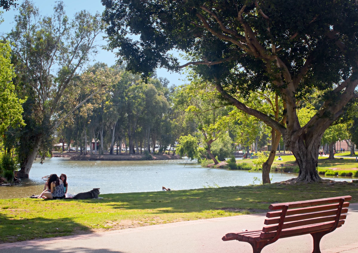 TEL AVIV, ISRAEL - May 6 2016: Lake, bench, girls with dog, and relax in Yarkon Park; Shutterstock ID 698891233; Your name (First / Last): Lauren Keith; GL account no.: 65050; Netsuite department name: Online Editorial; Full Product or Project name including edition: Tel Aviv Online Update