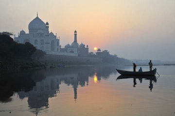 Boat paddling past Taj Mahal on Yamuna River.