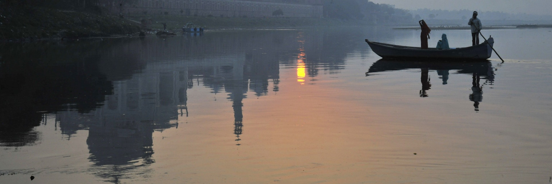 Boat paddling past Taj Mahal on Yamuna River.
