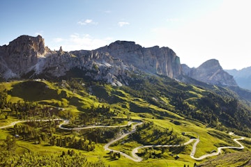 Overview of road winding through valley below Italian Alps.