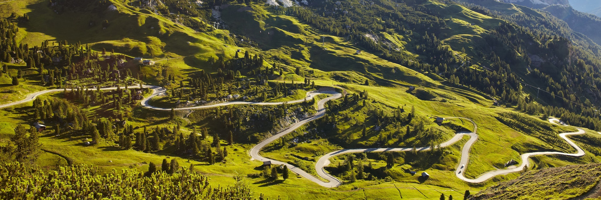 Overview of road winding through valley below Italian Alps.