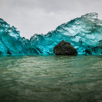 blue iceberg with rocks inside, under rain