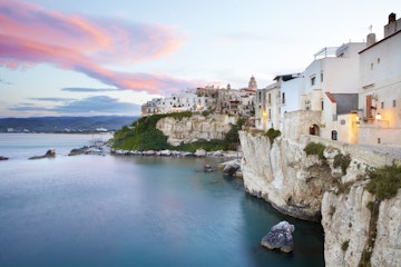 Sun setting on medieval town of Vieste perched on cliff ridge.