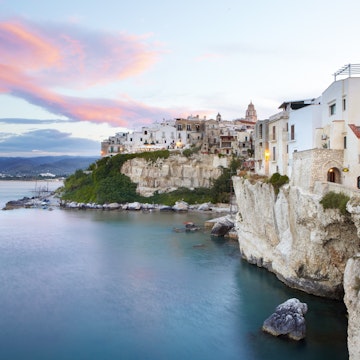 Sun setting on medieval town of Vieste perched on cliff ridge.