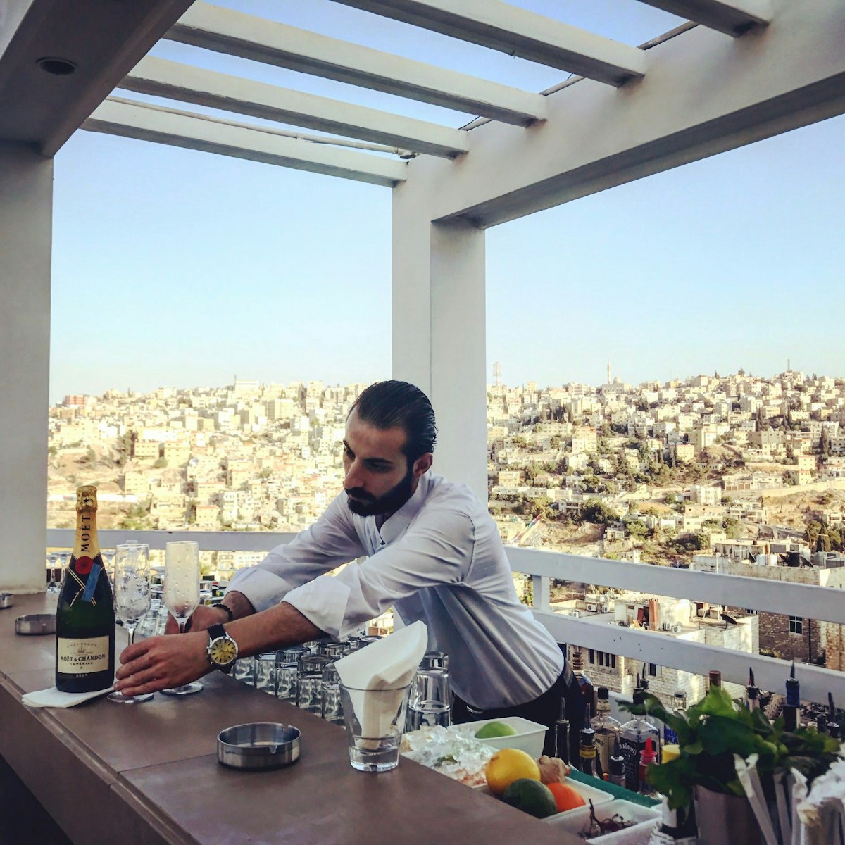 Bartender Amin serving champagne, with a view of Amman from Cantaloupe's upper terrace