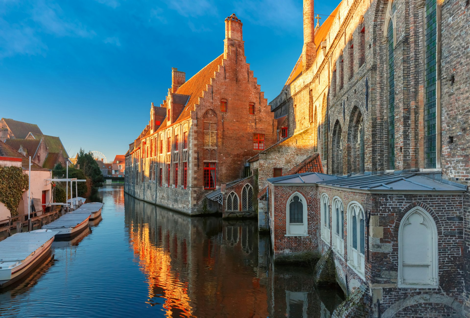 The exterior of the Museum Sint-Janshospitaal against the canal on a calm, blue-skied winter morning in Bruges, Belgium
