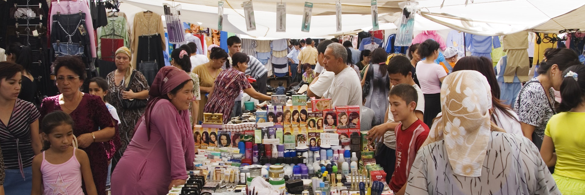 People walking around woman selling cosmetics and personal hygiene products at covered stall at Chorsu Bazaar.