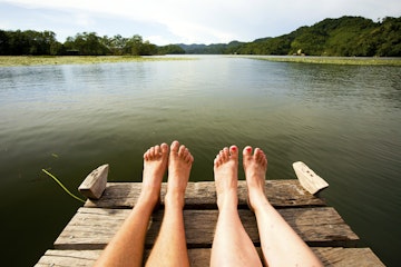 View of couple's feet sitting on river jetty.