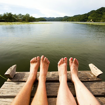 View of couple's feet sitting on river jetty.