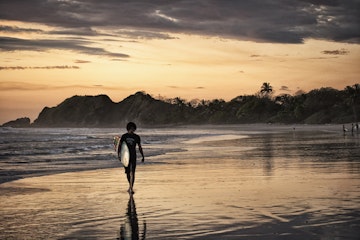 Surfer on beach at sunset.