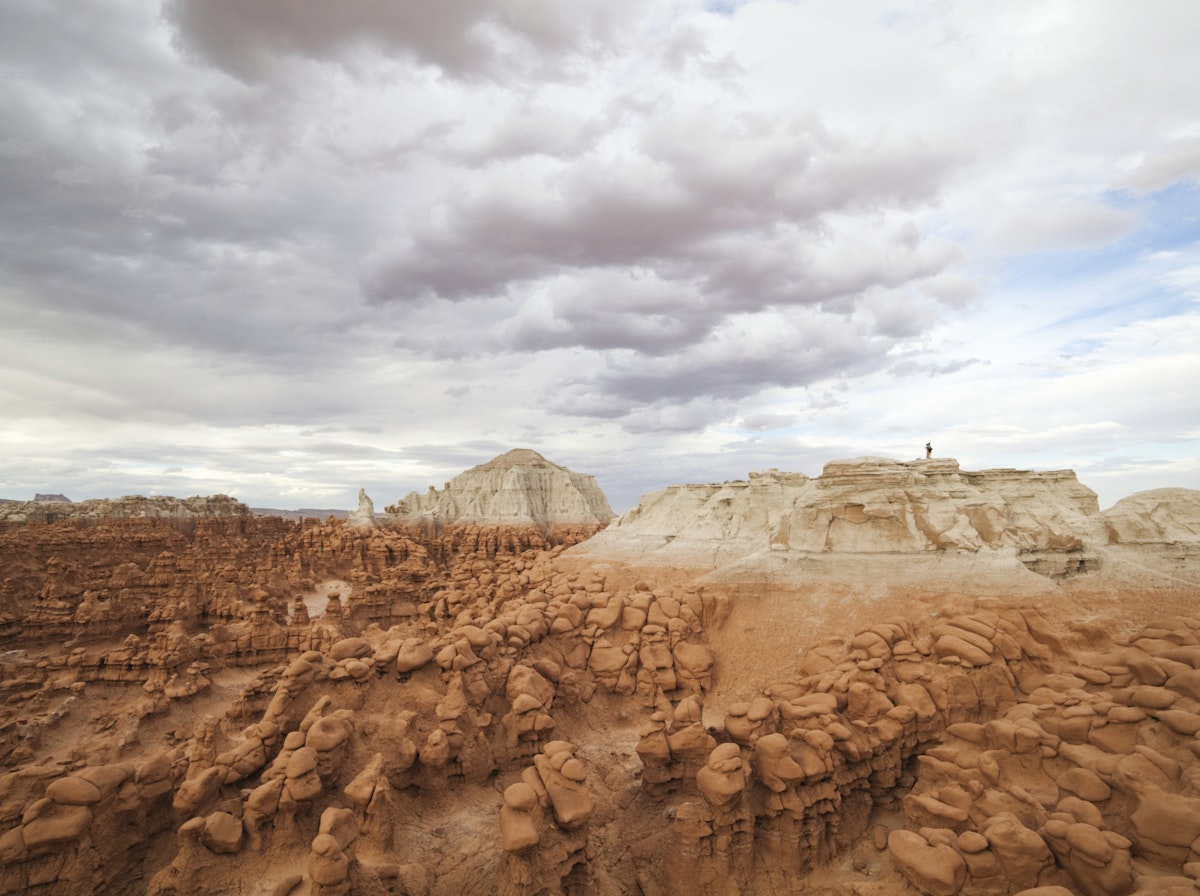 Hikers stand on the summit of a high mesa overlooking the vast field of hoodoos at Goblin Valley State Park, Utah.