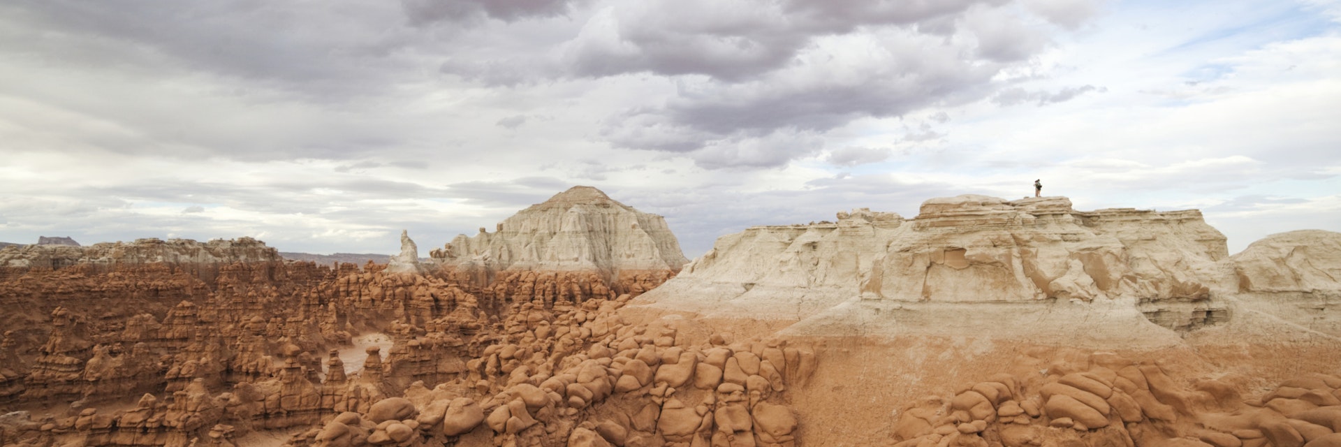 Hikers stand on the summit of a high mesa overlooking the vast field of hoodoos at Goblin Valley State Park, Utah.