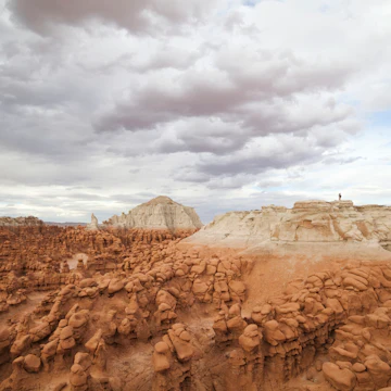 Hikers stand on the summit of a high mesa overlooking the vast field of hoodoos at Goblin Valley State Park, Utah.