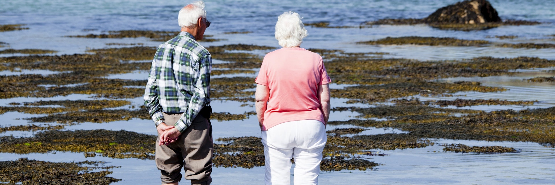Elderly couple standing in shallows looking towards Cromwell Castle on Tresco Island.