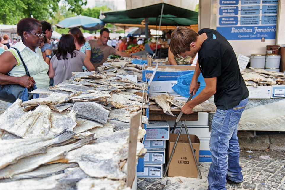 Barcelos, Portugal - August 23, 2012: A man is cutting bacalhau during the market day. Bacalhau dishes are very common in Portugal.; Shutterstock ID 241520329; Your name (First / Last): Tom Stainer; GL account no.: 65050 ; Netsuite department name: Online Editorial; Full Product or Project name including edition: Best in Travel 2018