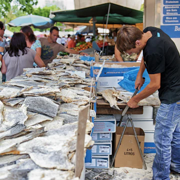 Barcelos, Portugal - August 23, 2012: A man is cutting bacalhau during the market day. Bacalhau dishes are very common in Portugal.; Shutterstock ID 241520329; Your name (First / Last): Tom Stainer; GL account no.: 65050 ; Netsuite department name: Online Editorial; Full Product or Project name including edition: Best in Travel 2018