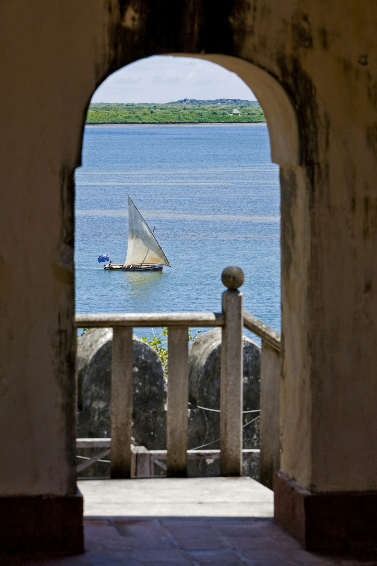 Kenya, Lamu Island, Lamu. A sailing boat (mashua) framed in an arch of Lamu Fort, which is now a museum.