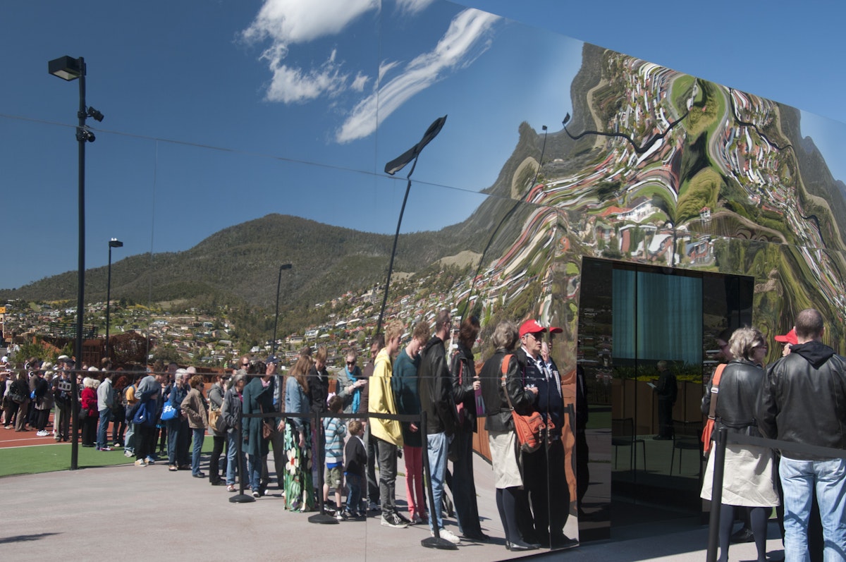 Visitors queuing to enter MONA, the Museum of Old and New Art, reflected in the building's mirror glass.