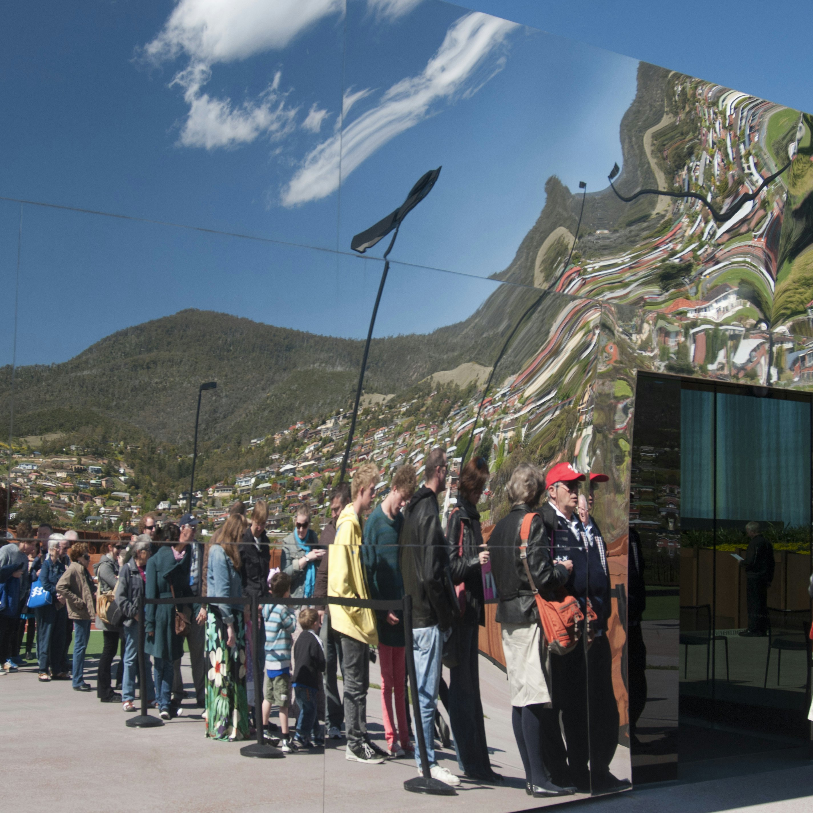 Visitors queuing to enter MONA, the Museum of Old and New Art, reflected in the building's mirror glass.