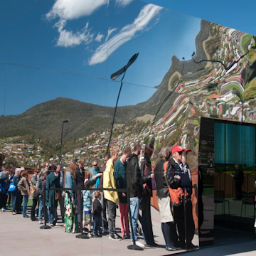 Visitors queuing to enter MONA, the Museum of Old and New Art, reflected in the building's mirror glass.