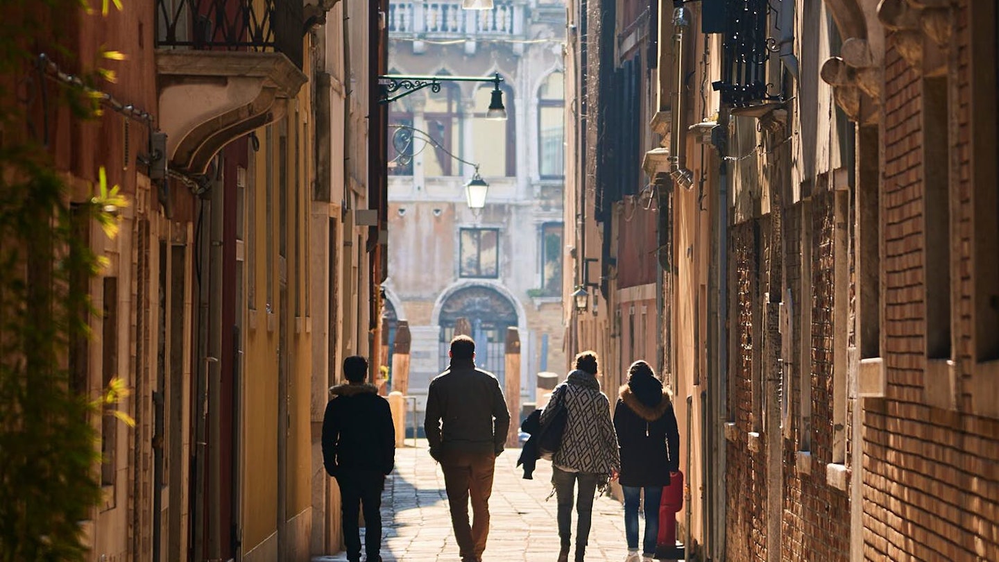 A group of people walk through a narrow alleyway in Venice