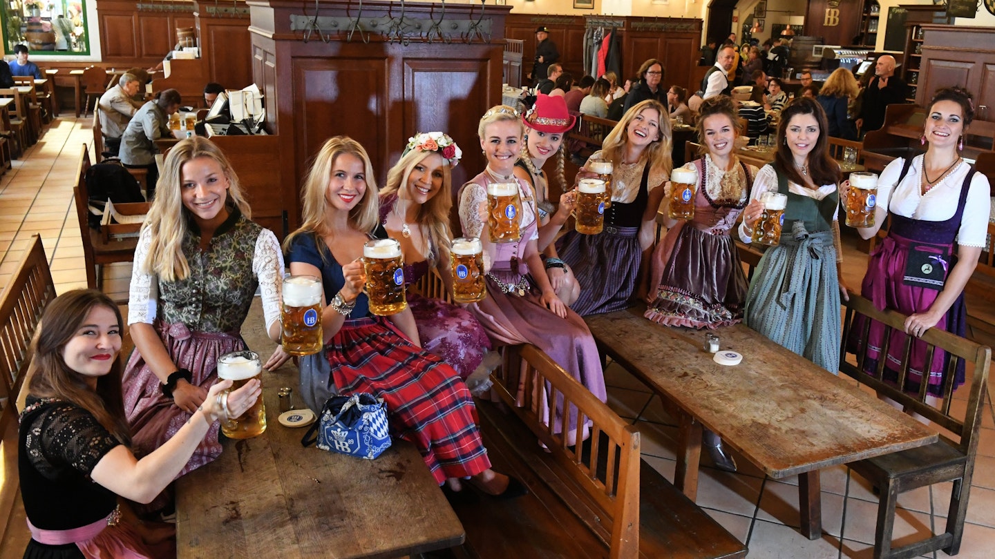 Women hold beer steins in traditional German outfits.