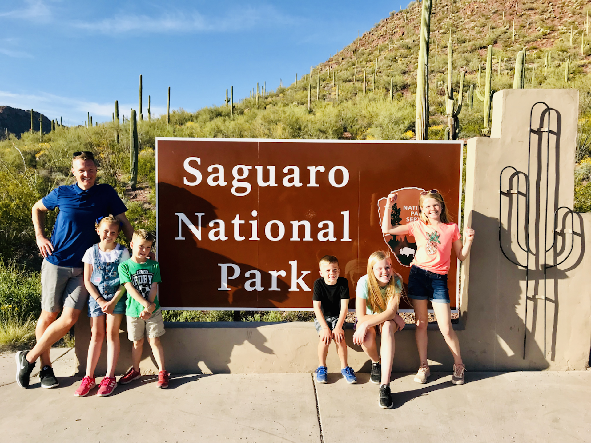 A family with small children stands in front of the entrance sign for Saguaro National Park
