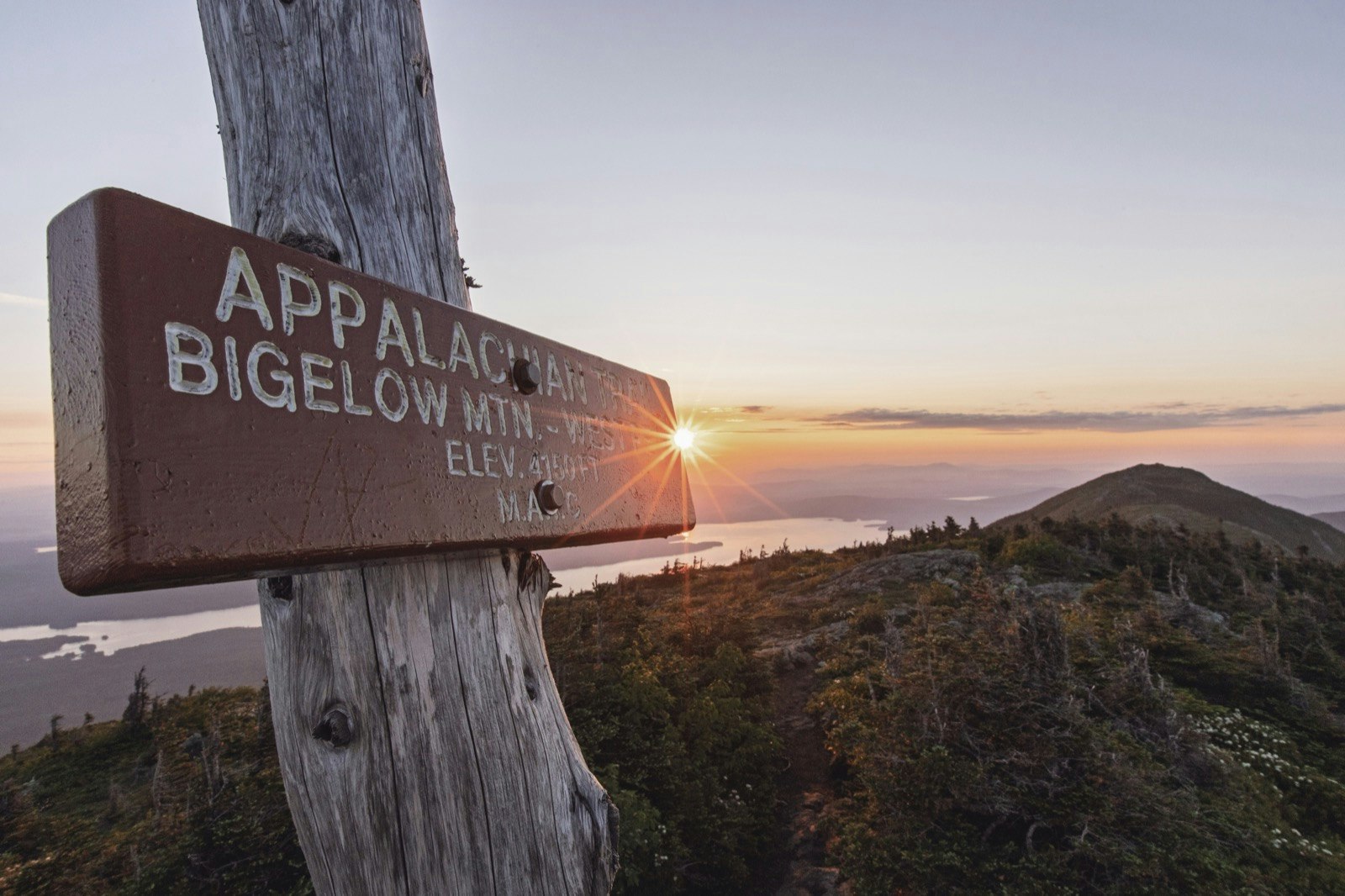 A sign reading Appalachain Trail - Bigelow Mountain, with a sunset in the background