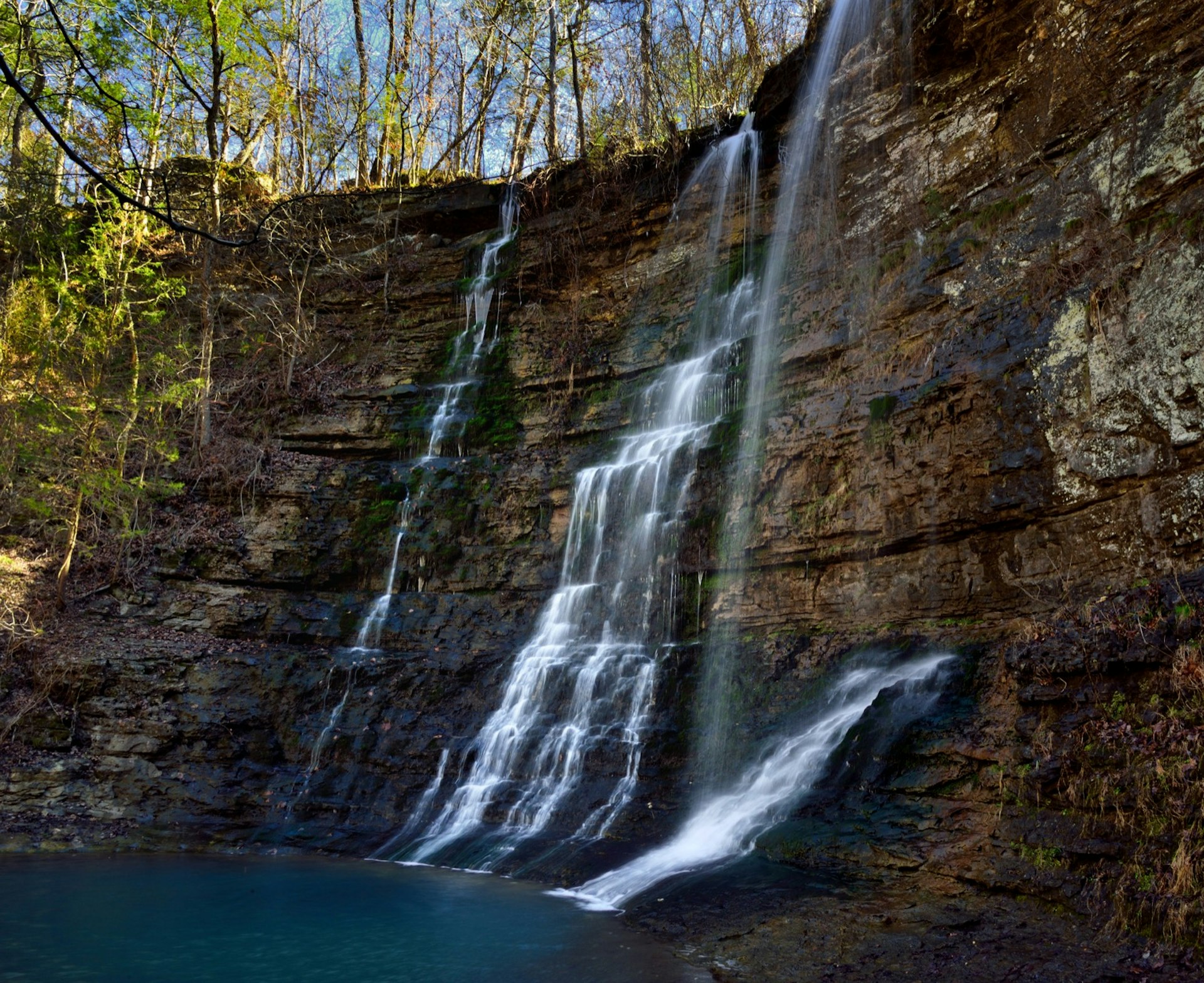 A waterfall trickles across dark rock into a pool below