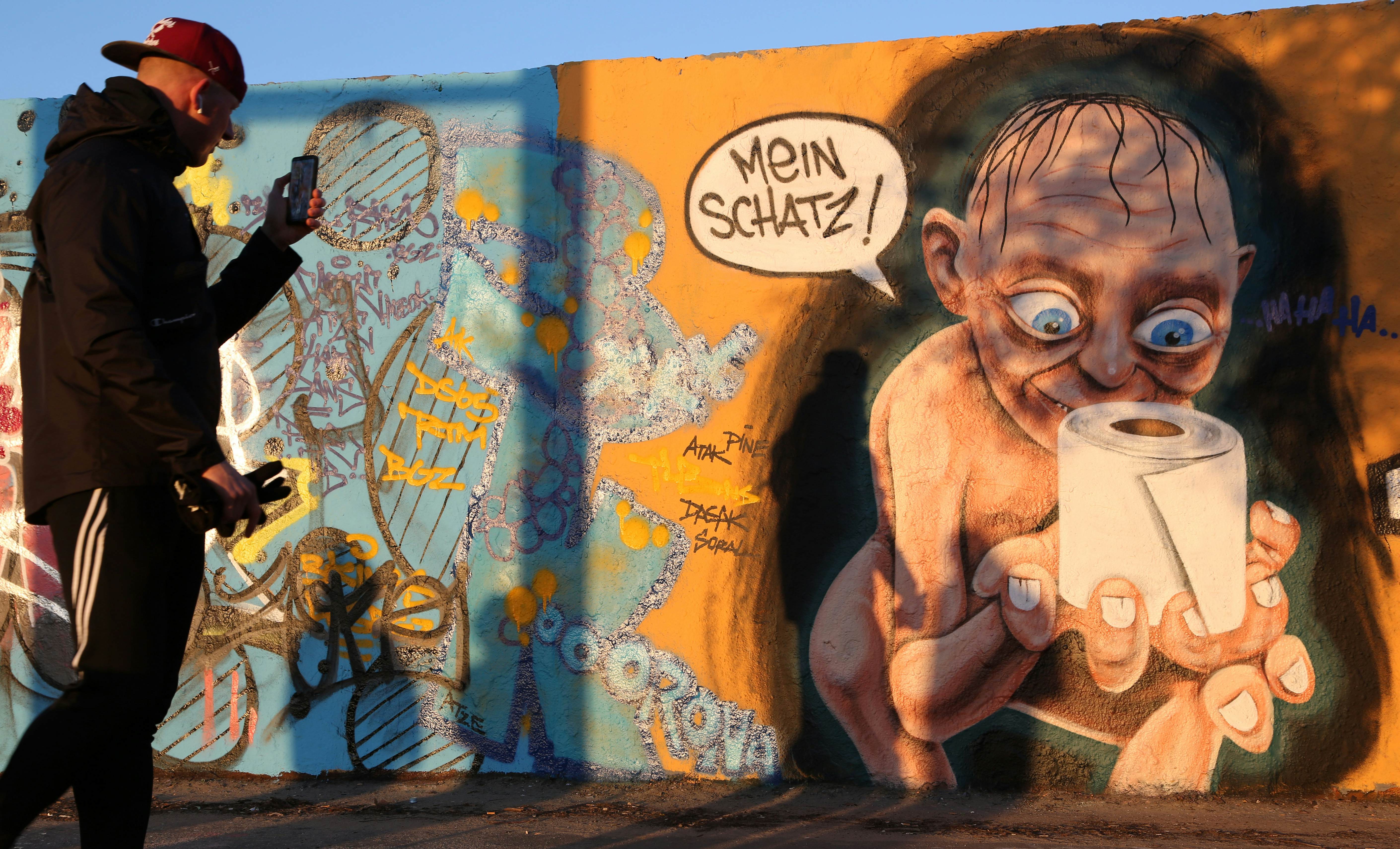 A visitor takes a photo of graffiti featuring the Lord of the Rings character Gollum holding a roll of toilet paper, a shopping item hoarded by consumers during the coronavirus pandemic crisis, and the words "My Treasure" in German