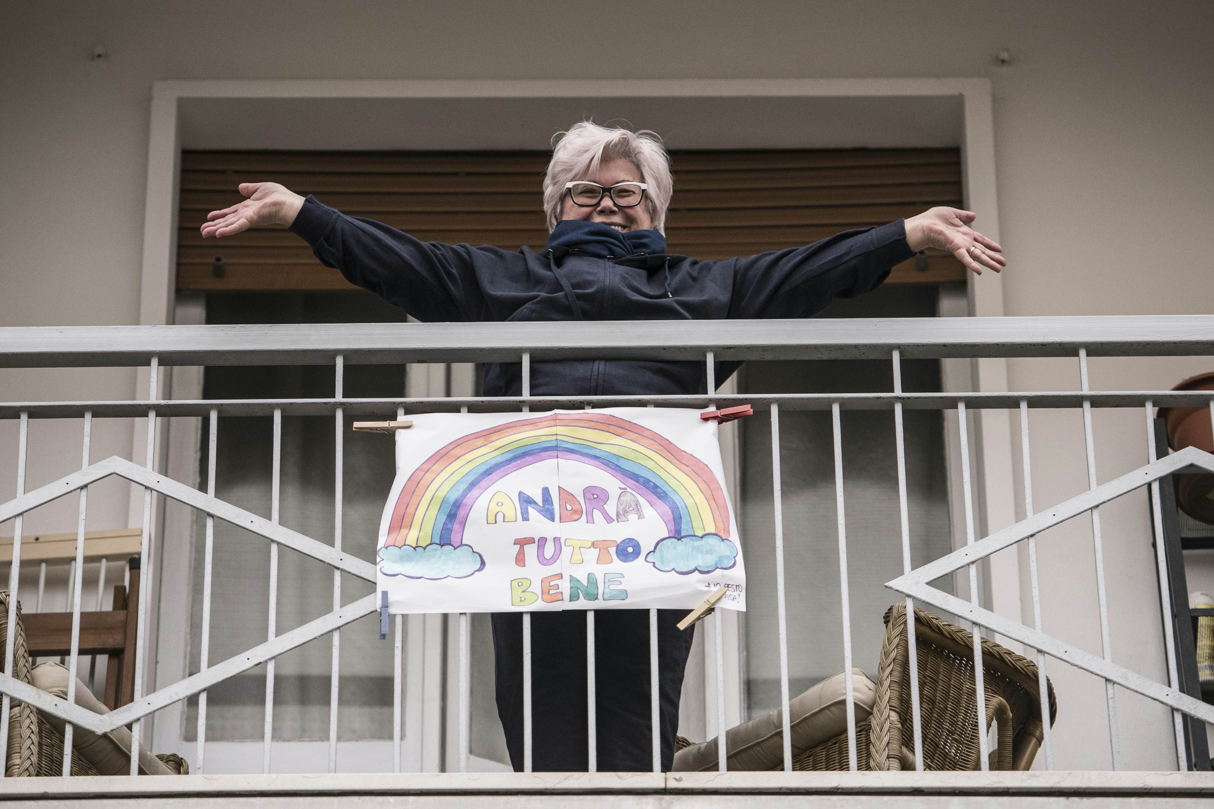 A woman smiles and gestures above poster that says "Everything will be fine" during a flash mob to raise morale 