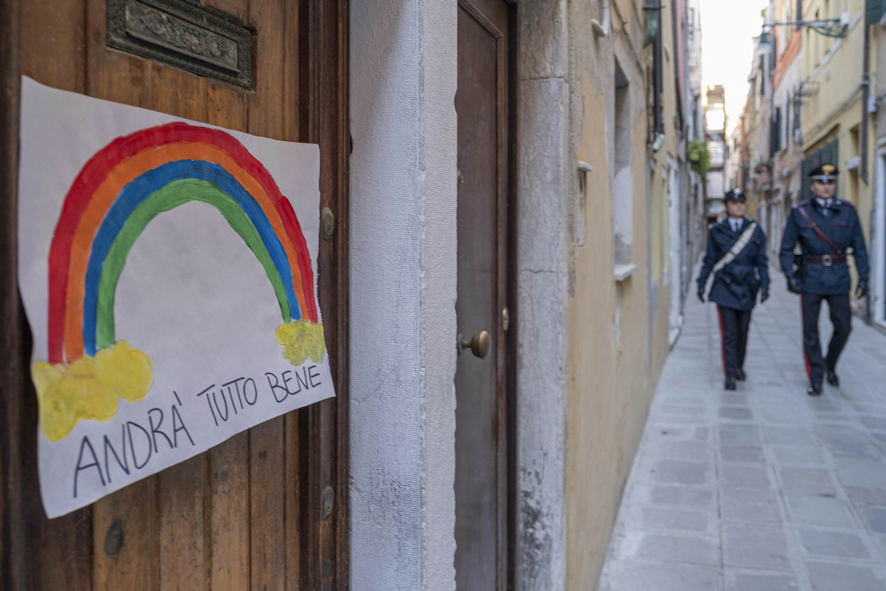 Carabinieri walk in a calle, in the door is attached a poster with the inscription: everything will be fine 