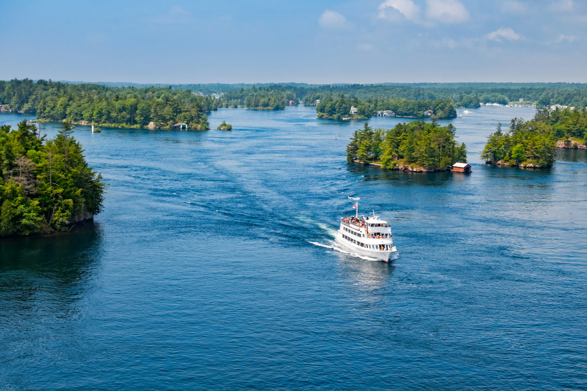 An aerial shot of a tour boat cutting through a vast body of water littered with greenery-covered islands