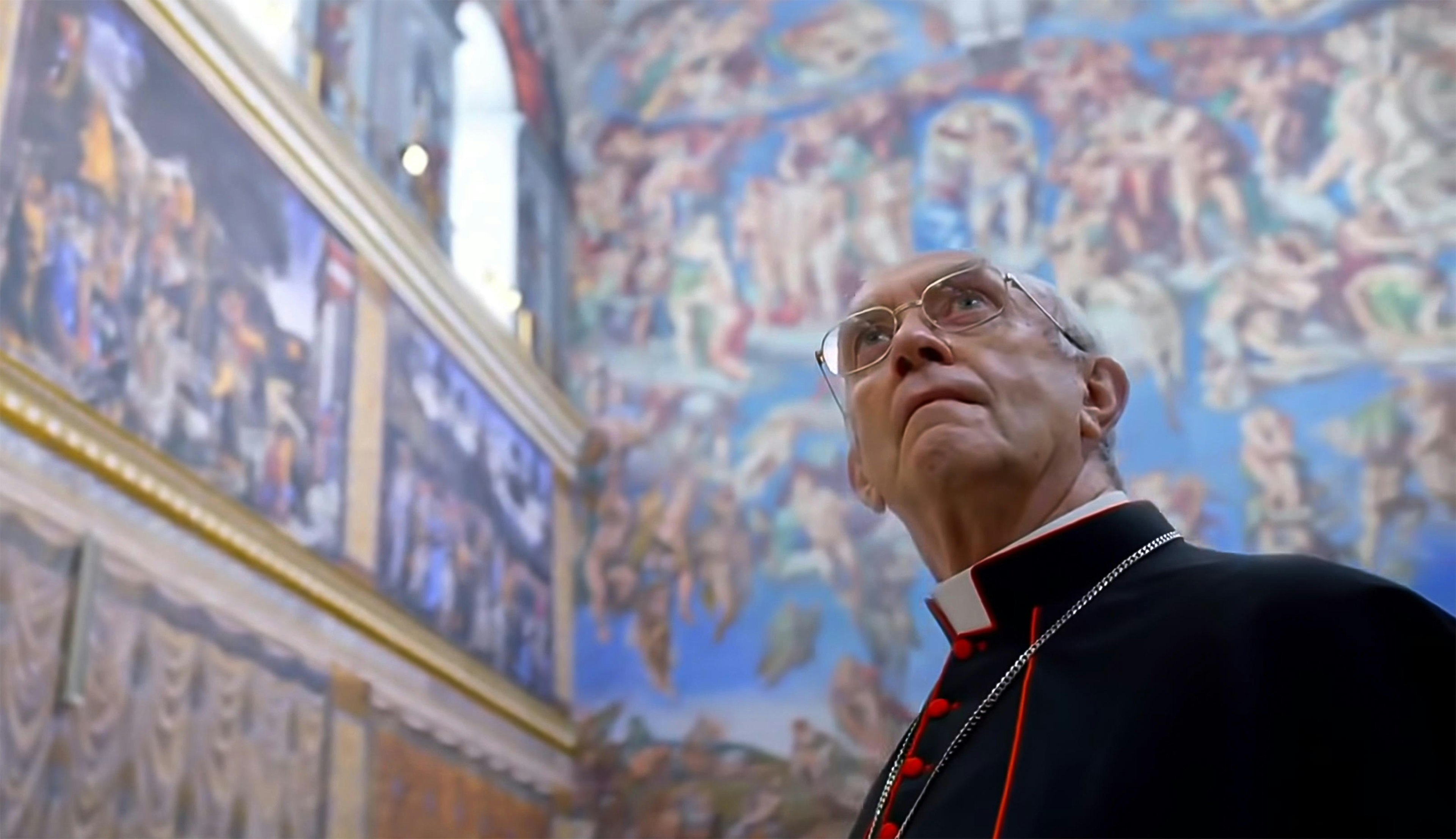 A man dressed as a pope stands in a room with walls and ceiling covered in intricate frescoes