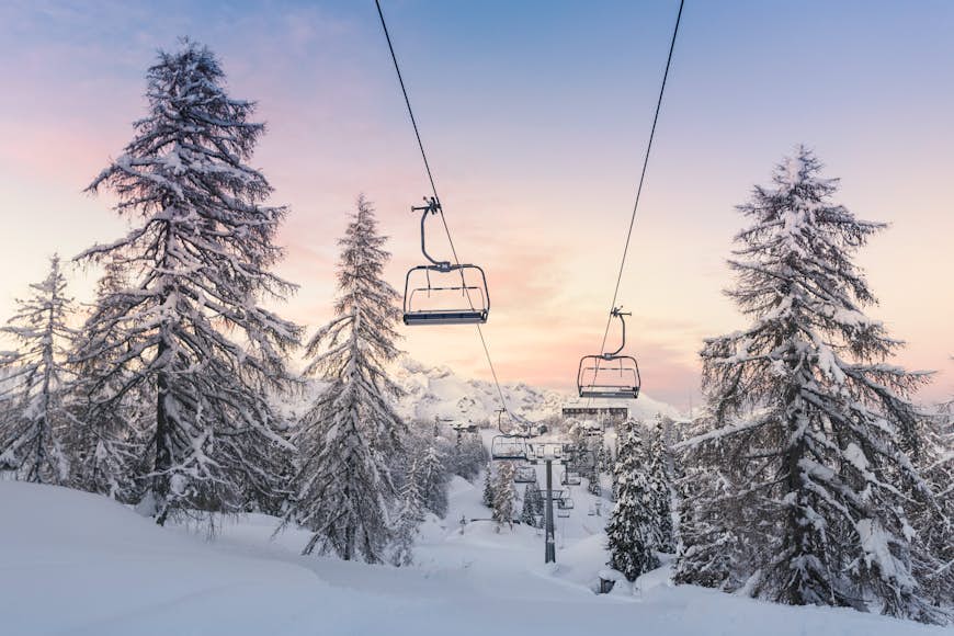 Empty ski lift chairs against a pink and purple sky