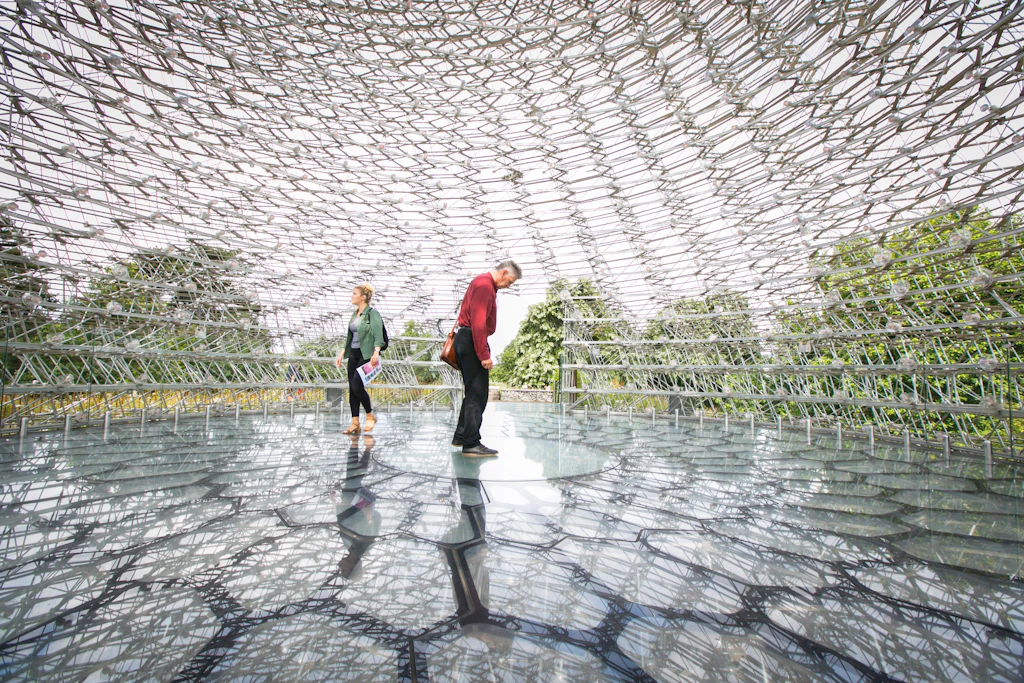 Two people stand in a large metal sculpture surrounded by honeycomb shapes