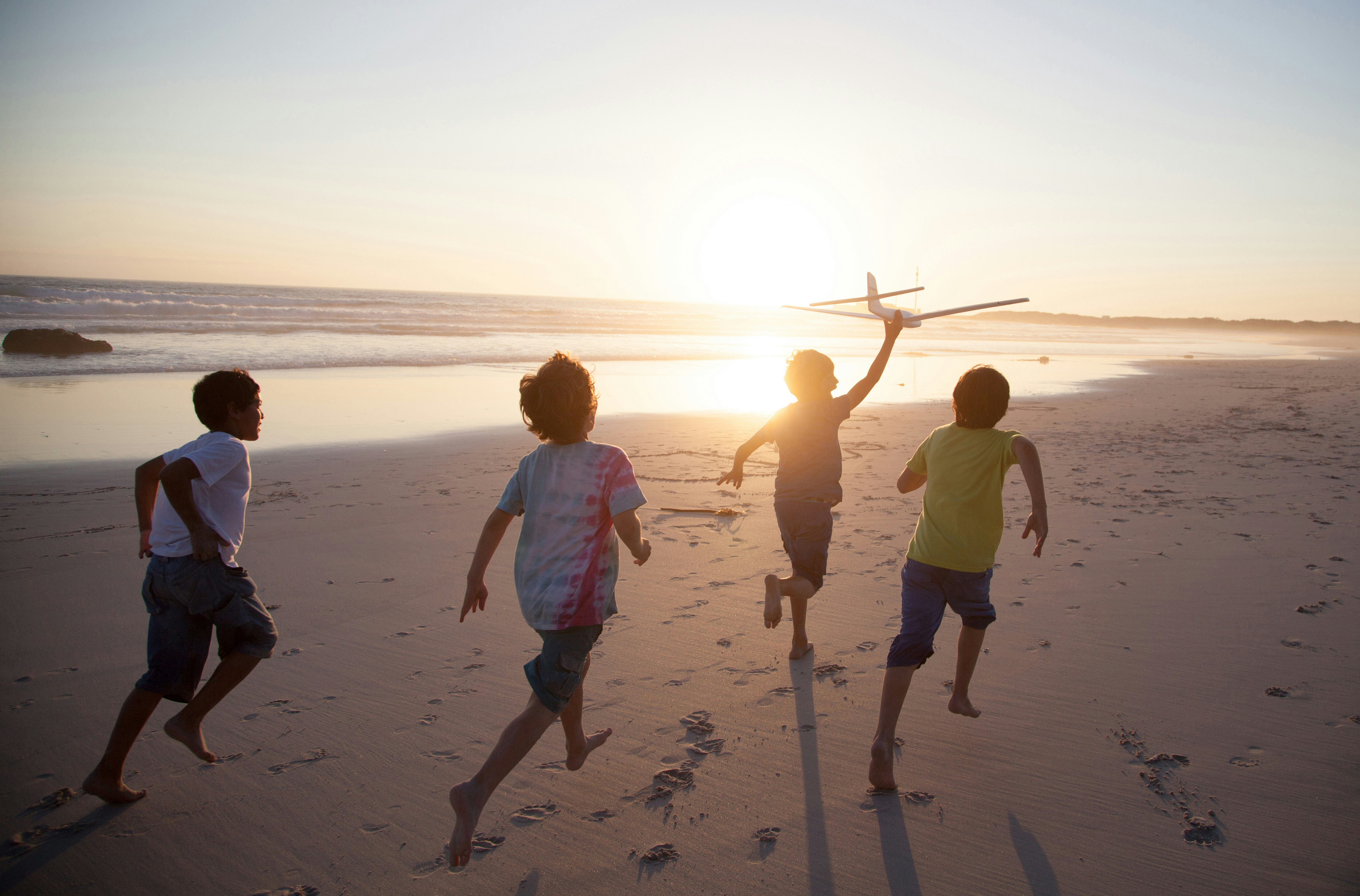 Boys running along beach with a toy plane