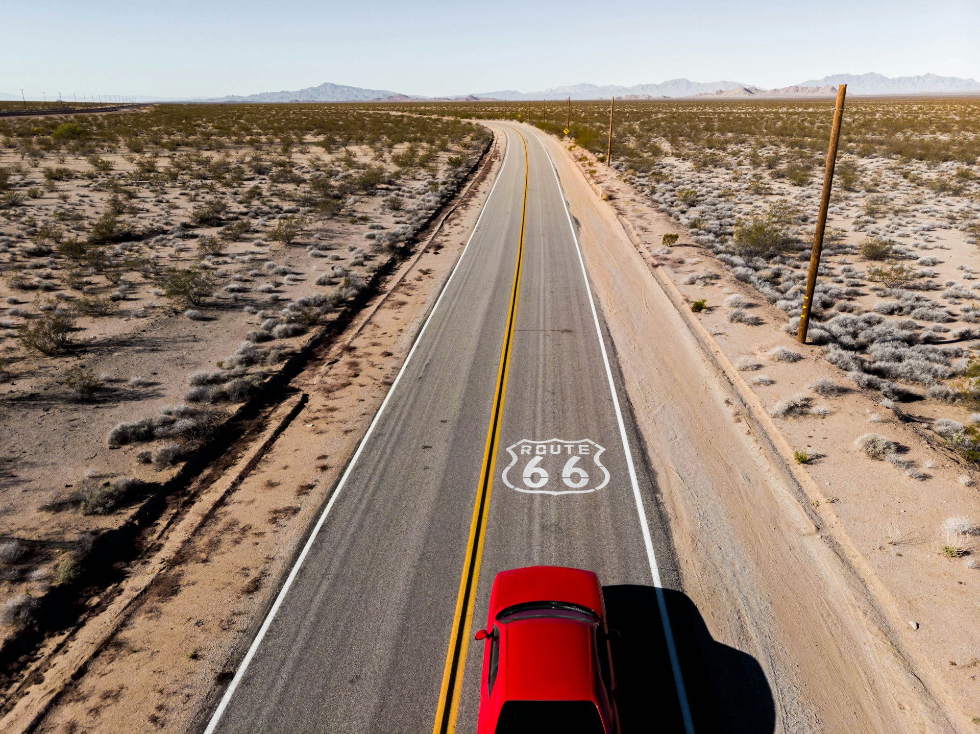 Drone view of American car driving in a straight road at the California desert.