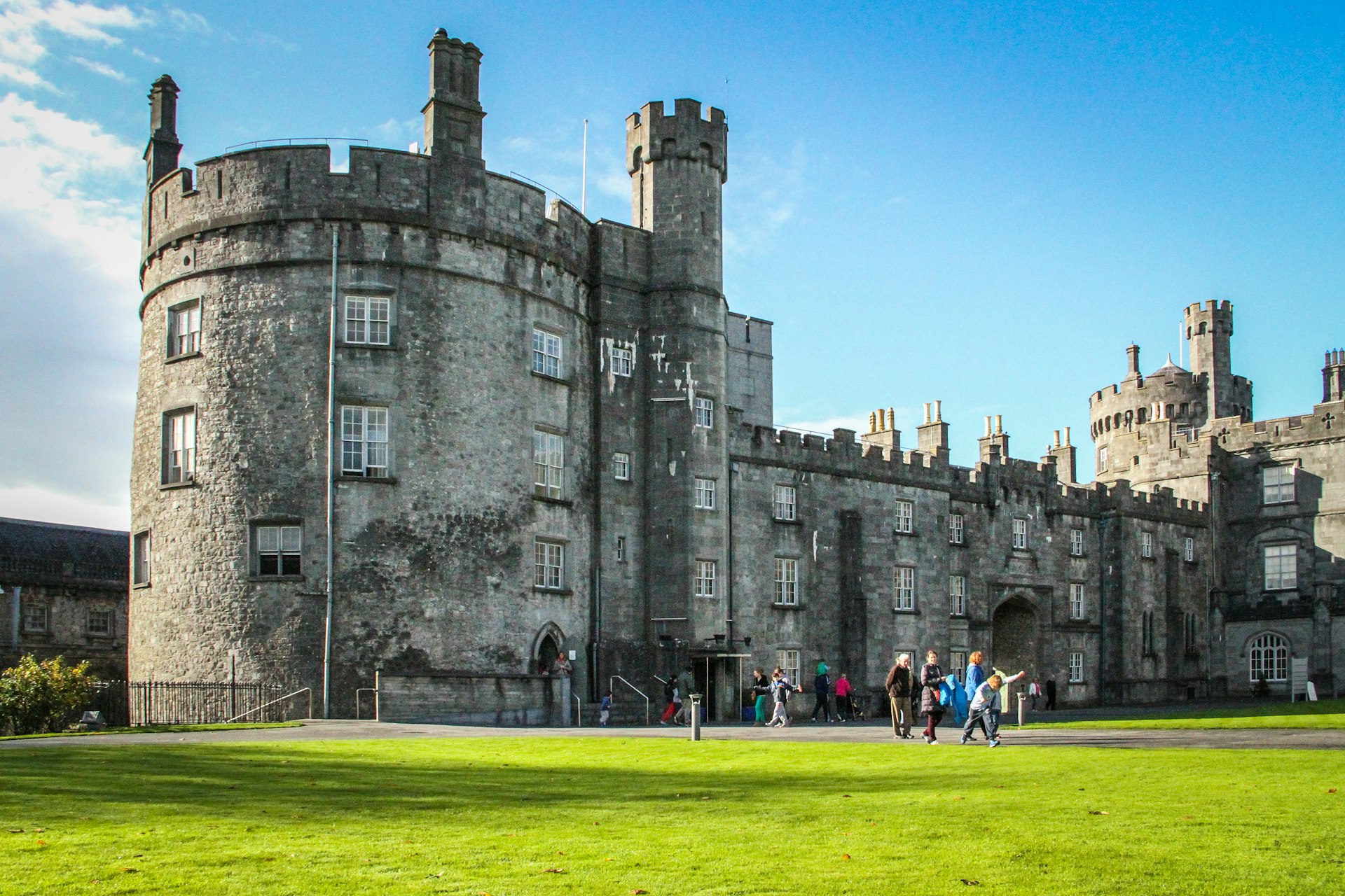 People walking by the left wing of the Kilkenny Castle in Ireland