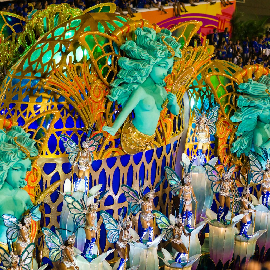 Rio de Janeiro, Brazil - February 17th, 2015: Women participating in Samba Parade are dancing samba on top of lavishly decorated parade float. Parade float depicts a fairy with the mirror. All participants are wearing elaborate costumes. Multitude of spectators is clearly visible.
