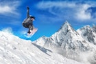 Snowboarder jumping high in the air with snow-capped mountains in the background. 