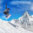 Snowboarder jumping high in the air with snow-capped mountains in the background. 