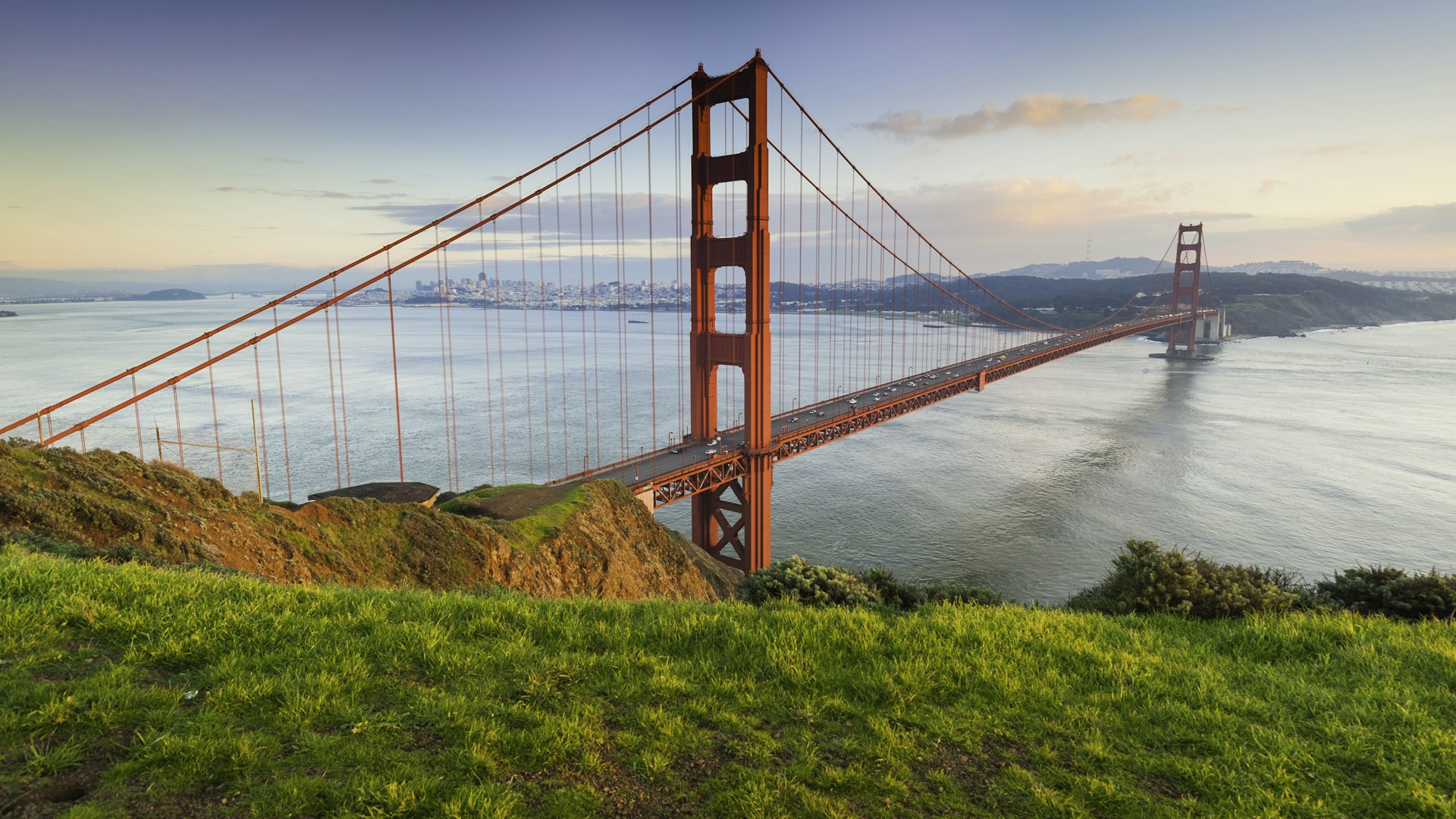 The Golden Gate Bridge as seen from the Marin County Headlands on a sunny clear day, with bright green grass in the foreground