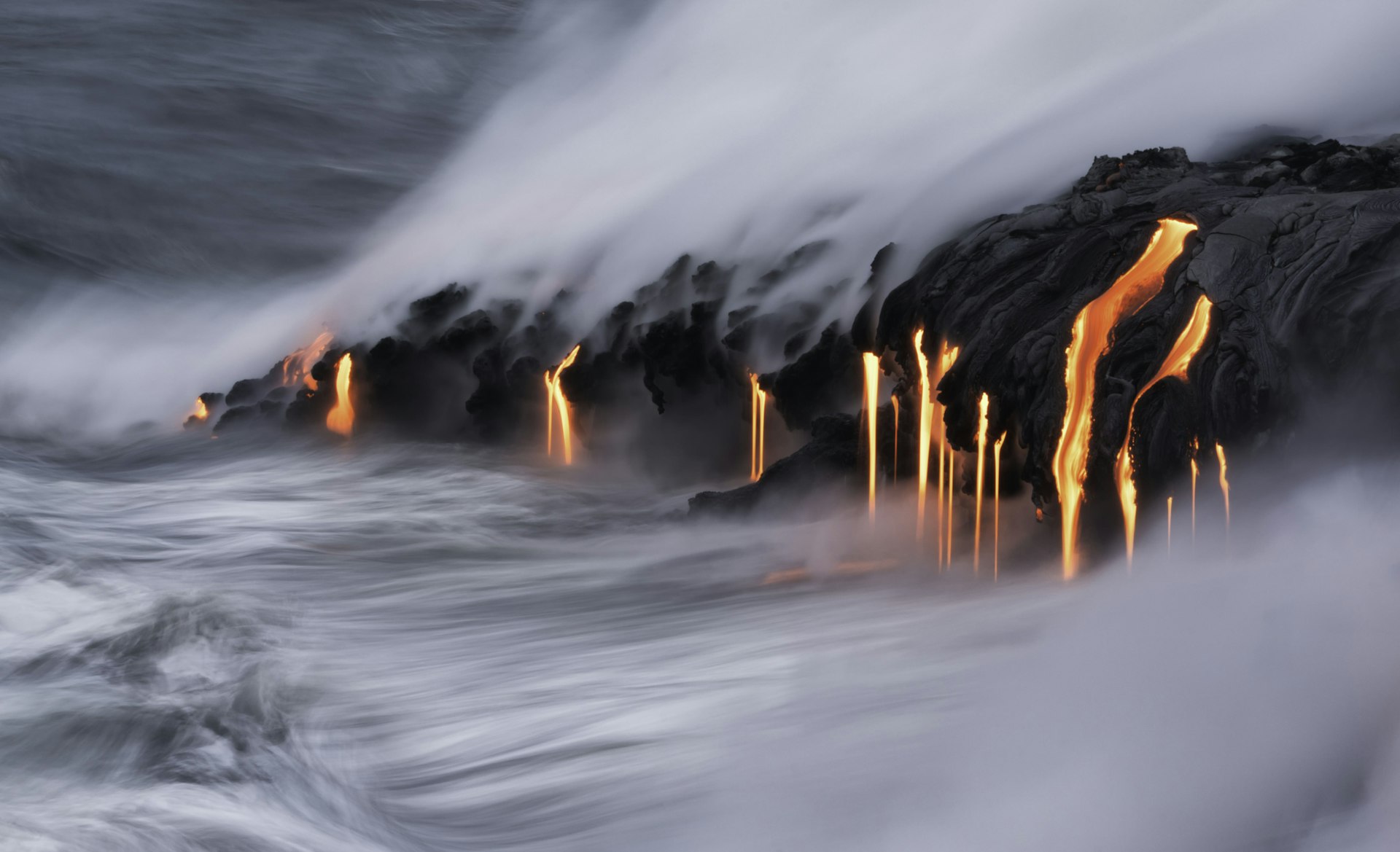 red lava drips into the ocean from a dark rock