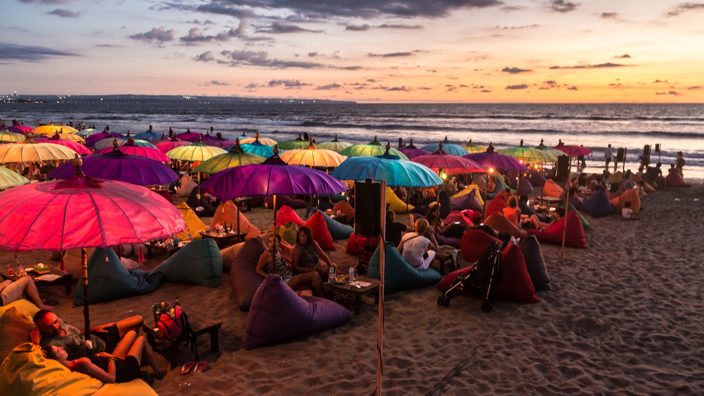 February 19, 2016: A crowd of people share food and drink under colourful umbrellas during sunset on Kuta beach.
